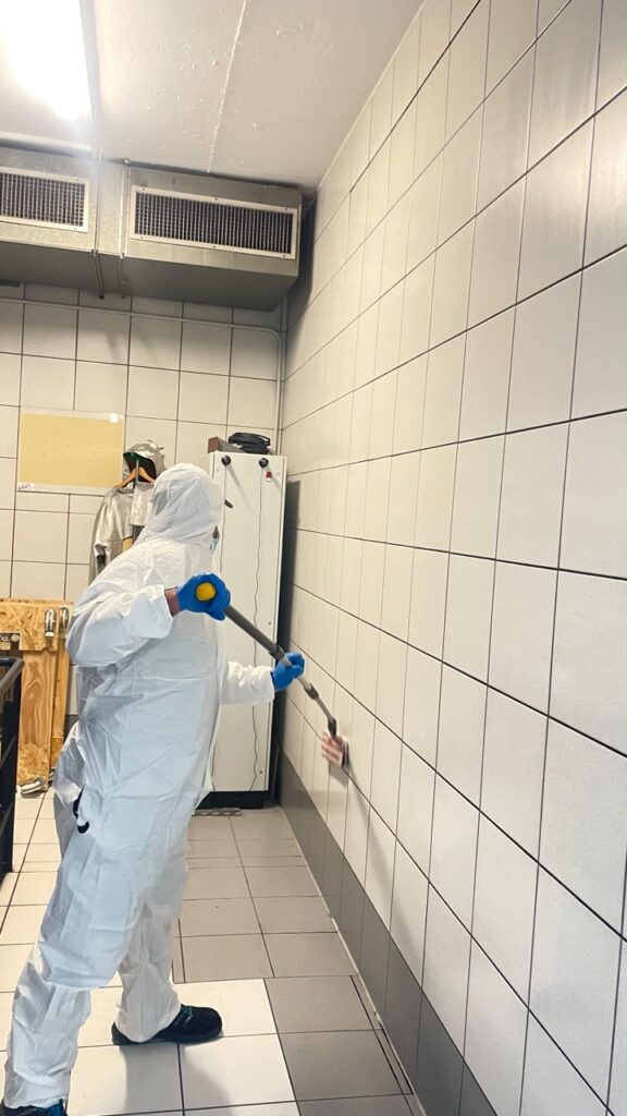 Mitarbeiter in Schutzkleidung bei der Reinigung einer gefliesten Wand